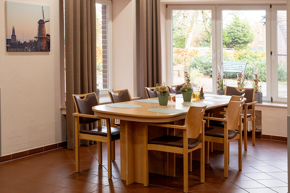 Gemütlicher Aufenthaltsraum mit großem Tisch, acht Stühlen, Fensterfront mit Blick ins Grüne und herbstlicher Tischdekoration.