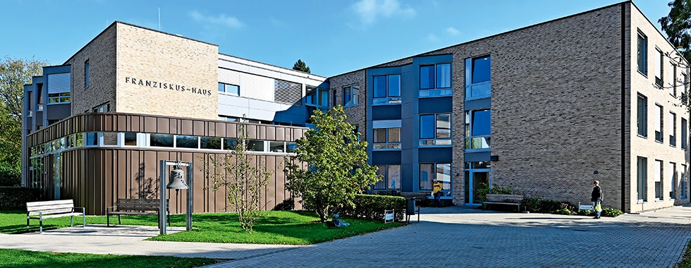Pflegeeinrichtung mit dem Schriftzug „Franziskus-Haus“, moderner Bau mit hellen und dunklen Backsteinfassaden, großem Eingangsbereich, Gehweg und Grünflächen.