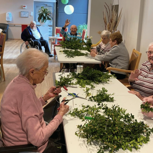 Bewohnerinnen und Bewohner im Franziskus-Haus Kleve binden gemeinsam Palmzweige in geselliger Runde.