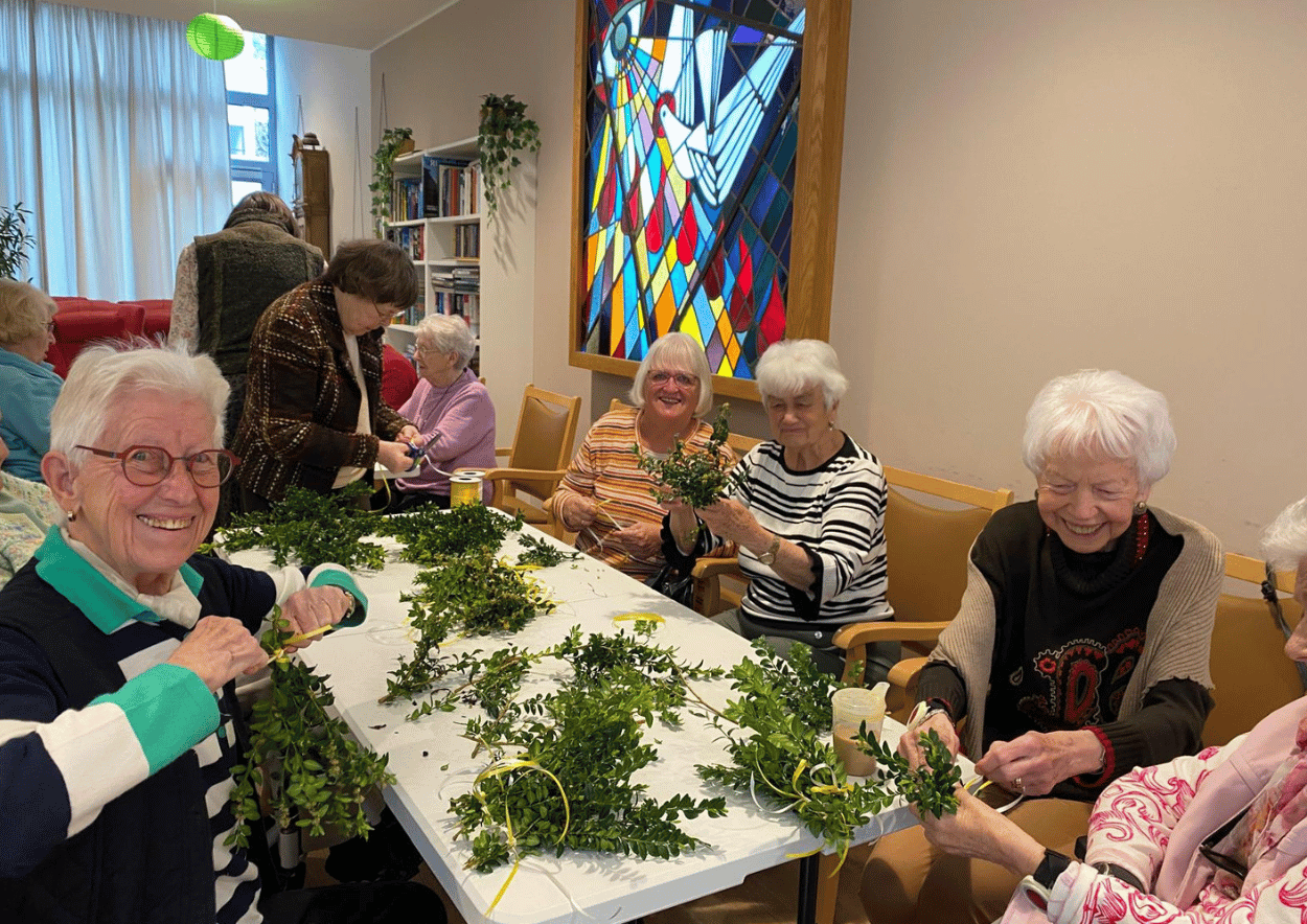Bewohnerinnen und Bewohner im Franziskus-Haus Kleve binden gemeinsam Palmzweige in geselliger Runde.