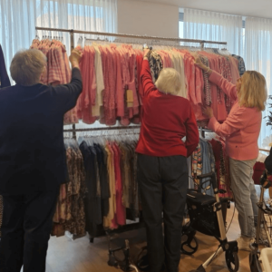 Bewohnerinnen stöbern gemeinsam mit einer Mitarbeiterin des Modemobils durch die Frühlings- und Sommerkollektion im Veronika-Haus