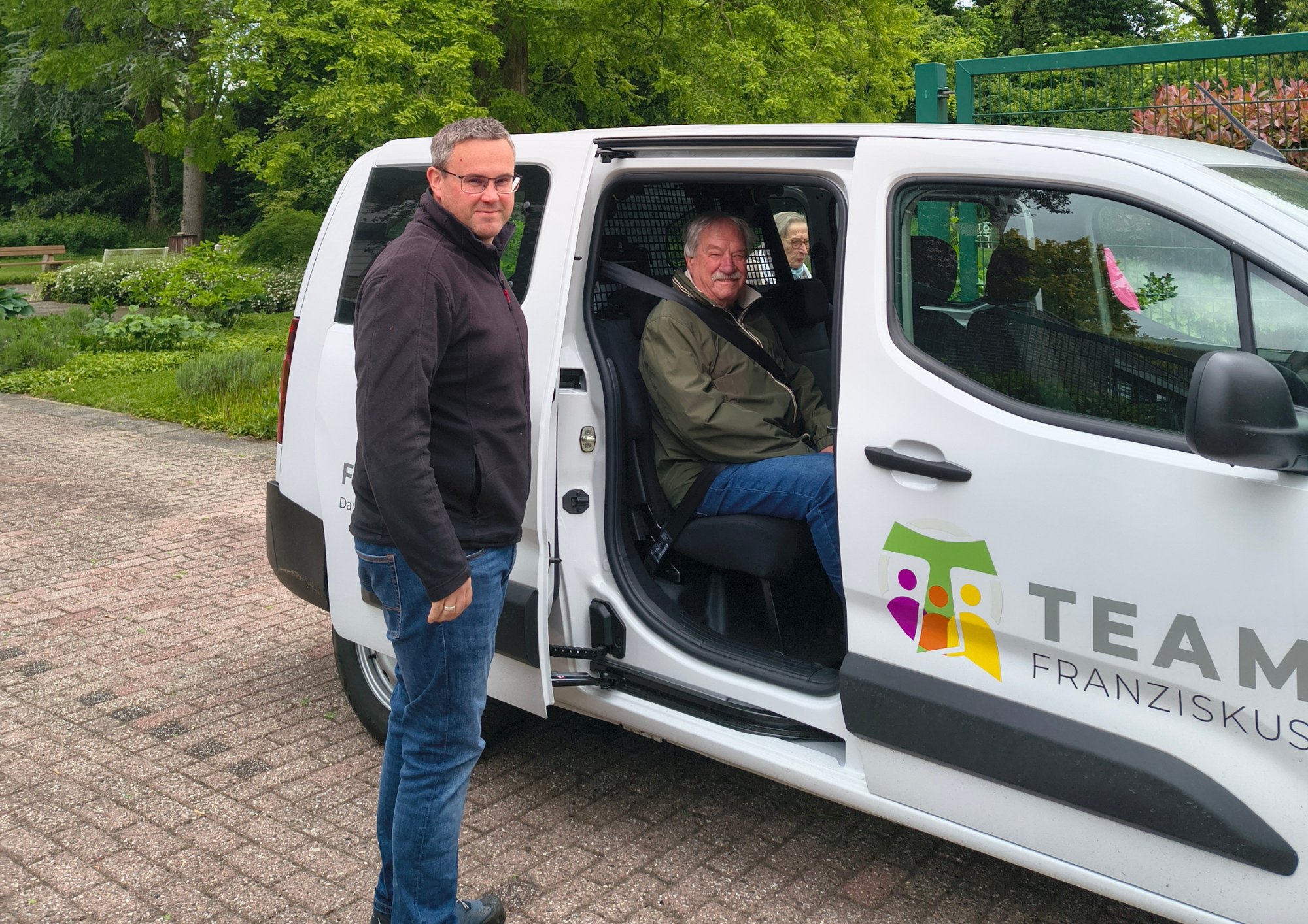 Bewohner steigen mit Unterstützung eines Mitarbeiters in einen Fahrzeug des Team Franziskus für einen Ausflug ein.