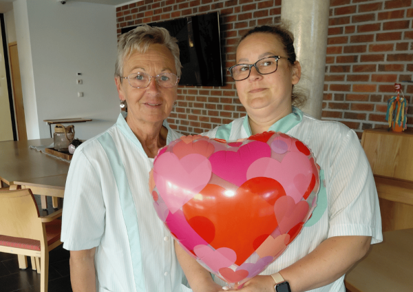 Zwei Mitarbeitende im Regina Pacis Haus Kevelaer halten einen Herzluftballon im Aufenthaltsraum zum Tag der Pflege
