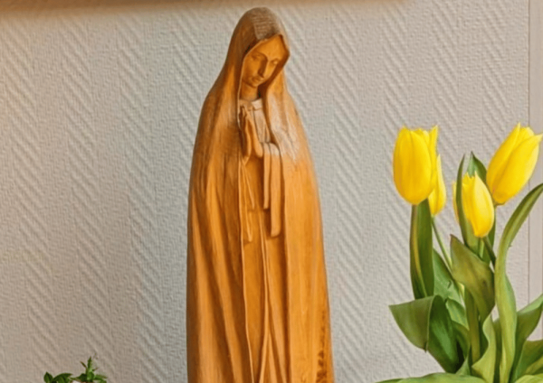Holzfigur der betenden Maria neben gelben Tulpen vor neutralem Hintergrund, als religiöses Symbol der Wallfahrt im St. Elisabeth-Haus Xanten