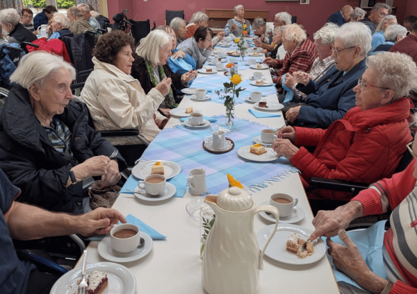 Teilnehmende der Domwallfahrt aus dem St. Elisabeth-Haus Xanten sitzen gemeinsam an einer langen Kaffeetafel mit Kuchen und Getränken im Haus der Begegnung