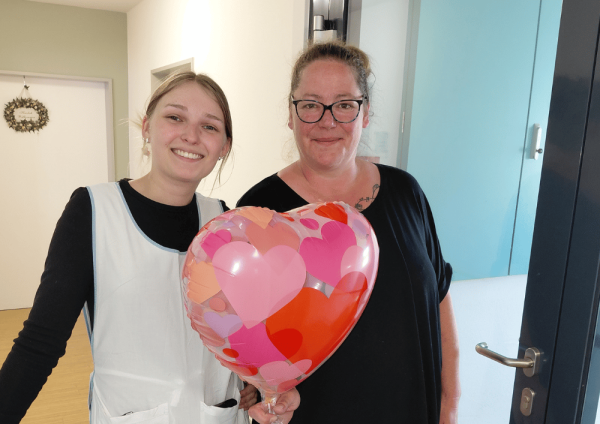 Zwei Mitarbeitende im Regina Pacis Haus Kevelaer stehen im Flur und halten einen Herzluftballon zum Tag der Pflege in der Hand