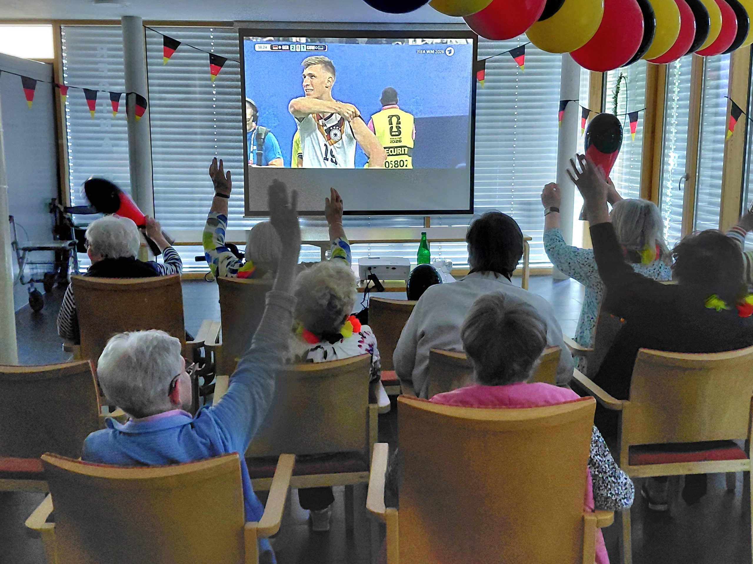 Bewohner schauen gemeinsam das WM-Spiel Deutschland gegen Curacao auf einer Leinwand im Regina Pacis Haus.