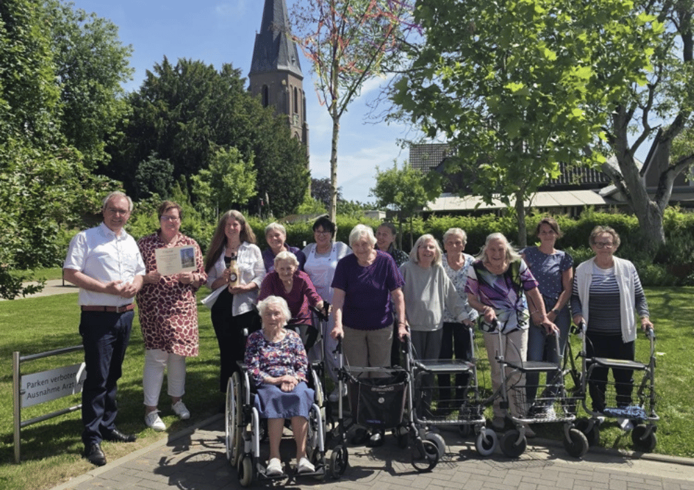 Gruppenfoto von Bewohnern und Mitarbeitenden mit Urkunde im Garten der Einrichtung