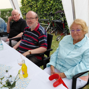 Bewohner und Bewohnerinnen sitzen gemeinsam am Tisch und genießen Getränke beim Sommerfest.