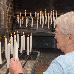 Seniorin zündet in einer Kirche eine Kerze an.