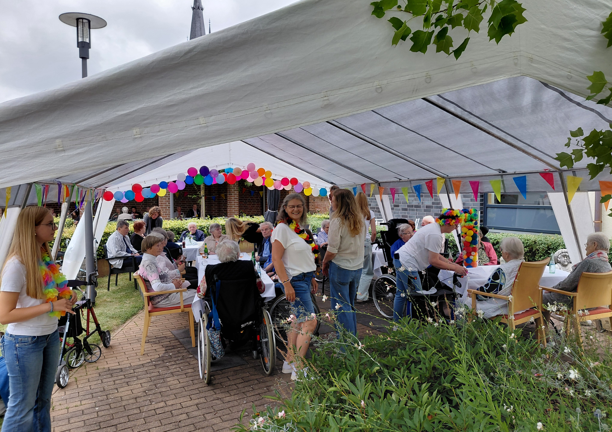 7 Sommerfest im Innenhof mit Bewohnerinnen, Bewohnern und Mitarbeitenden unter einem festlich geschmückten Pavillon.