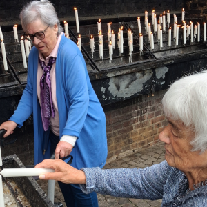 Zwei Seniorinnen entzünden gemeinsam Kerzen in einer Kirche.
