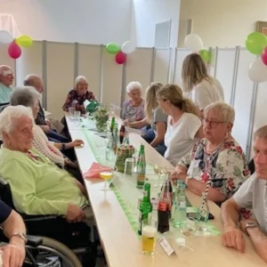 Eine Gruppe aus Bewohnerinnen, Bewohnern und Mitarbeitenden sitzt gemeinsam an einer langen Festtafel.