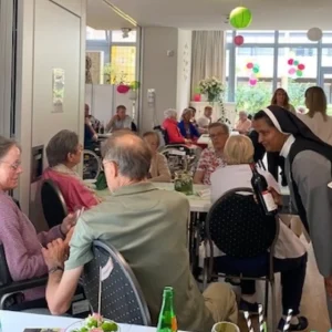 Eine Ordensschwester schenkt einem Gast an der voll besetzten Festtafel ein Getränk ein.