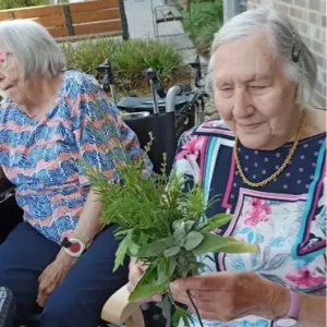 Eine ältere Frau sitzt auf der Terrasse und hält ein Bündel verschiedener frisch gesammelter Kräuter in den Händen.