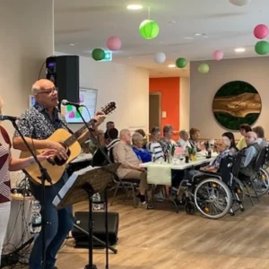 Ein Musiker mit Gitarre und eine Sängerin sorgen bei einer Feier vor den sitzenden Gästen für Livemusik.