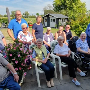 Eine Gruppe älterer Menschen und Begleitpersonen versammelt sich bei sonnigem Wetter für ein gemeinsames Foto im Garten.“
