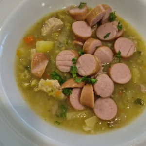 Ein Teller Gemüseeintopf mit Würstchenscheiben, Kartoffelstücken und gehackter Petersilie.