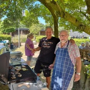 Zwei Männer stehen gemeinsam am Grill und bereiten das Essen für das Sommerfest zu.
