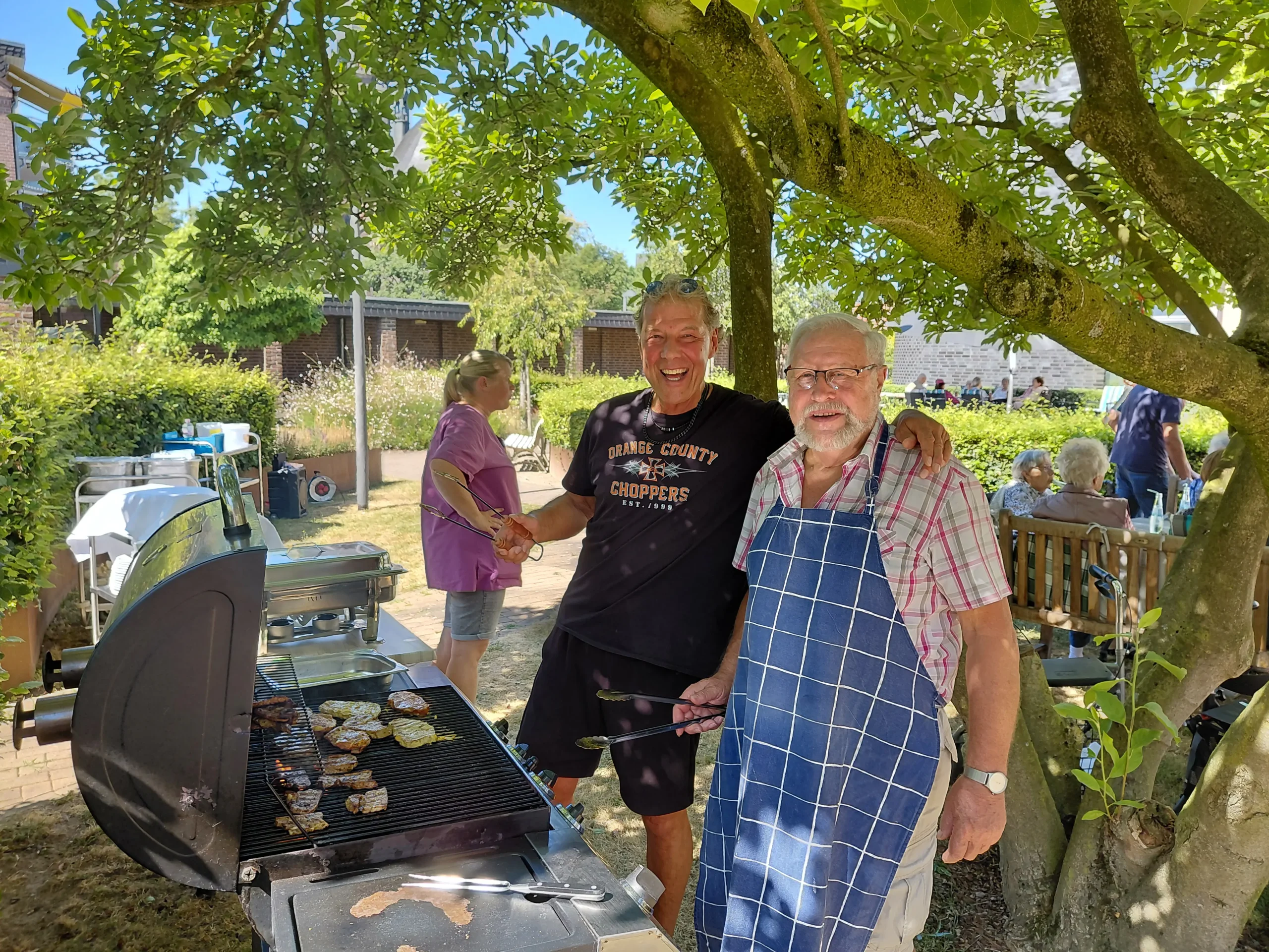 Zwei Männer stehen gemeinsam am Grill und bereiten das Essen für das Sommerfest zu.