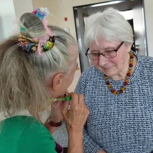 Eine Clownin mit Haarschmuck begegnet einer älteren Frau mit Brille aus nächster Nähe.