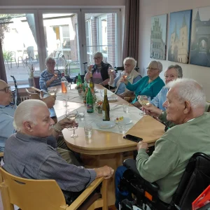 Eine Gruppe älterer Menschen sitzt an einem herbstlich gedeckten Tisch und hebt die Weingläser zum Anstoßen.