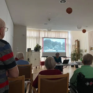 Publikum bei einem Vortrag zur Geschichte des Forstgartens in Kleve. Auf der Leinwand ist eine historische Aufnahme der Gartenanlage zu sehen.