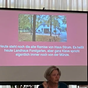 Vortrag zur Geschichte des Forstgartens in Kleve mit einer Aufnahme des heutigen Landhauses Forstgarten auf der Leinwand.