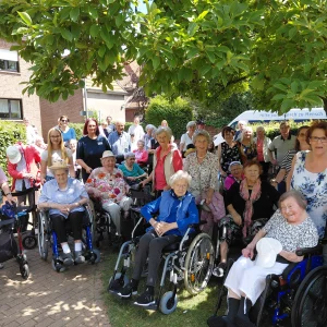 Eine große Gruppe älterer Menschen und Begleitpersonen posiert unter einem Baum, einige mit Rollstühlen und Rollatoren.