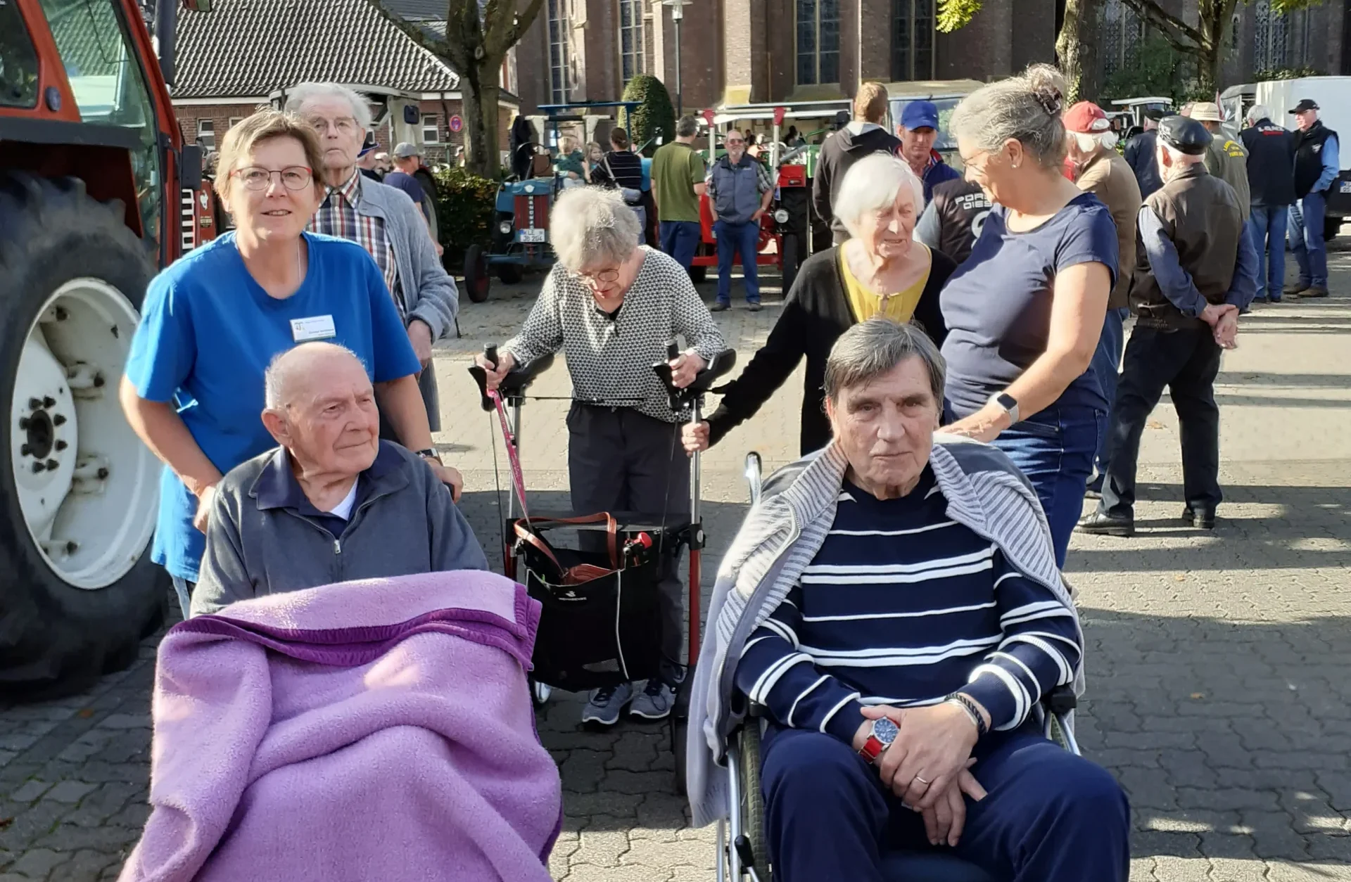 Gemeinsamer Besuch der Traktorenausstellung Ältere Menschen mit Rollstühlen und Rollator besuchen mit Begleitpersonen eine Traktorenausstellung vor einer Kirche.