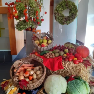 Erntedankdekoration mit Obst, Gemüse und Nüssen in Körben und auf Stroh, ergänzt durch Blumen und einen Kranz.