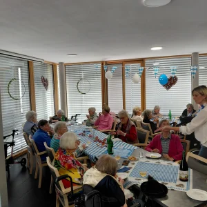 Gäste essen und unterhalten sich an blau-weiß gedeckten Tischen. Eine stehende Frau wendet sich einer Teilnehmerin zu.