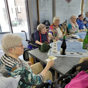 Ältere Frauen sitzen an einem blau-weiß dekorierten Tisch. Eine Frau im Vordergrund hält ein Glas.