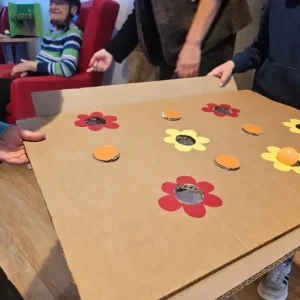 Kinder und Senioren spielen gemeinsam mit einem selbst gebastelten Geschicklichkeitsspiel aus Pappe und Blumenmotiven.