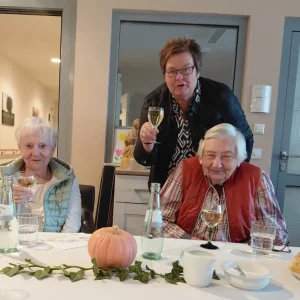 Zwei Seniorinnen und eine Mitarbeiterin halten Weingläser bei einer Feier an einer herbstlich dekorierten Tafel.