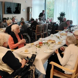 Bewohnerinnen und Bewohner eines Seniorenheims sitzen an gedeckten Kaffeetafeln und genießen Kuchen und Gespräche.