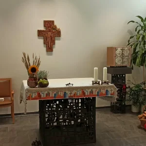 Ein Altar mit Kerzen und Sonnenblume unter einem Wandkreuz. Daneben liegen Erntegaben in Körben und auf Stroh.