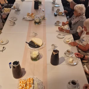 Blick über eine lange Tafel mit Torten und Kaffeekannen. Die Gäste trinken Kaffee und essen Kuchen.