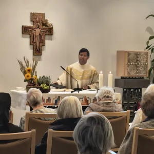 Ein Priester steht hinter dem mit Erntegaben und brennenden Kerzen geschmückten Altar. Davor sitzt die Gemeinde.
