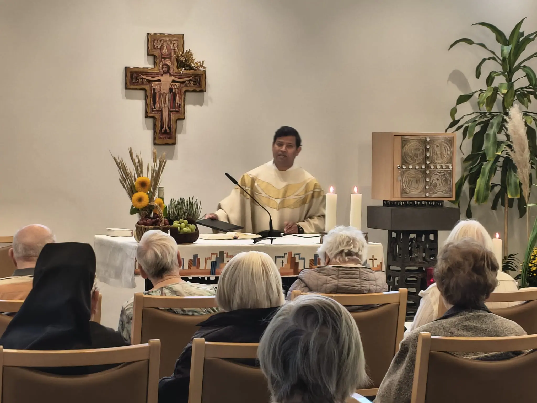 Ein Priester steht hinter dem mit Erntegaben und brennenden Kerzen geschmückten Altar. Davor sitzt die Gemeinde.
