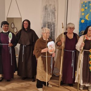 Sieben Darstellerinnen stehen in Kostümen mit Stäben und selbst gebastelten Tiermotiven vor einer Theaterkulisse.