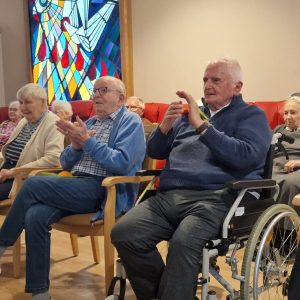 Seniorinnen und Senioren sitzen im Gemeinschaftsraum und applaudieren während einer Theateraufführung.