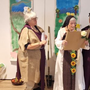 Vier Darstellerinnen in historischen Kostümen spielen eine Theaterszene vor einer bunt gestalteten Kulisse.