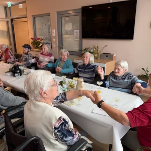 Seniorinnen sitzen gemeinsam an einer festlich gedeckten Tafel und halten sich während einer Feier an den Händen.