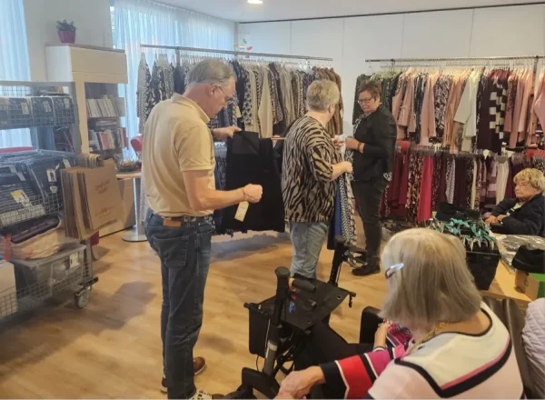 Ein Mann betrachtet eine Hose, während zwei Frauen beim mobilen Modeverkauf Kleidungsstücke auswählen und besprechen.