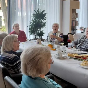 Seniorinnen und eine Mitarbeiterin sitzen an einer herbstlich dekorierten Kaffeetafel mit Kuchen im Seniorenheim.