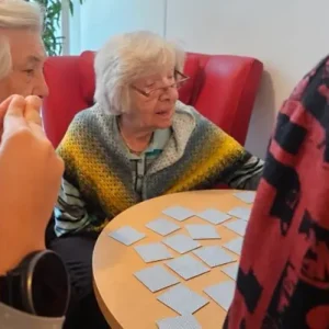 Zwei Seniorinnen sitzen mit Kindern an einem Tisch und spielen gemeinsam Memory mit verdeckten Spielkarten.